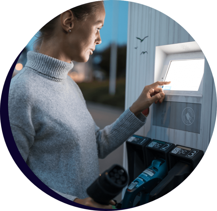 A lady at dusk using the touch screen of an electric car recharging station